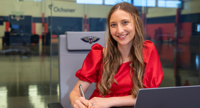 Alumni of the sport management degree program works at computer in the New Orleans Pelicans' practice arena.