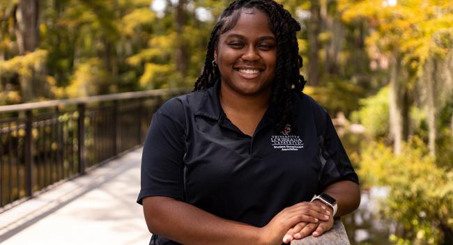 Onyeka Nwaezeapu smiling and wearing a student government association polo, standing near the UL Lafayette swamp.