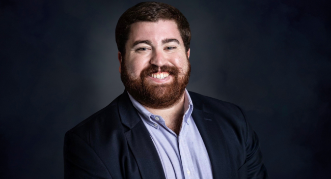 Graduate of UL Lafayette's MS in Accounting online program smiles for headshot in a blue button down and coat.