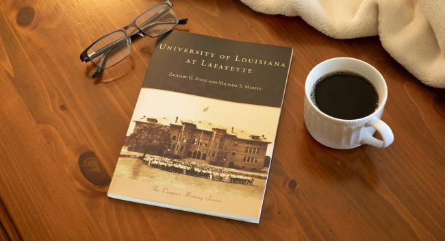 A book on a table with glasses and a cup of coffee.