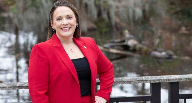 Amanda Devillier, alumna of UL Lafayette's MBA online, smiles for a portrait in front of Cypress Lake on campus.