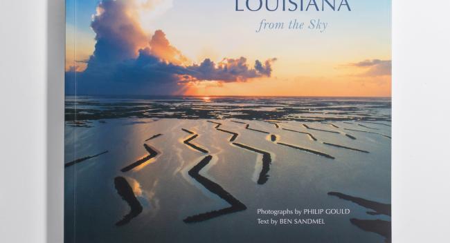 The cover of the book "Louisiana from the Sky" featuring an aeriel view of a flooded landsape and a setting sun through the clouds.