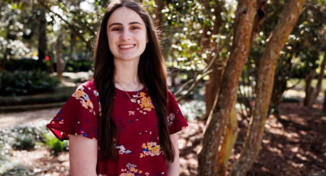 Portrait photograph of Bree Landry smiling in a burgundy blouse with a nature background.