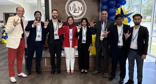 Eight people stand in front of a ULM sign holding up UL Lafayette hand signs.