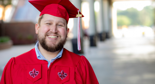 Jace Nugier smiles for a portrait in his red UL Lafayette mortarboard cap and gown.