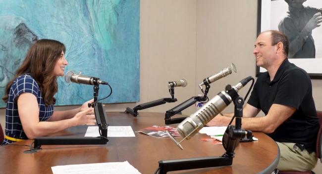 Two people sit across from each other in a recording studio.