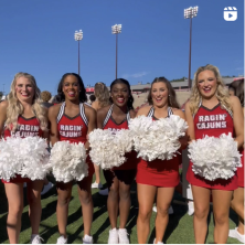 Ragin' Cajuns cheerleaders stand in a row with white pompoms lined up in front of them.