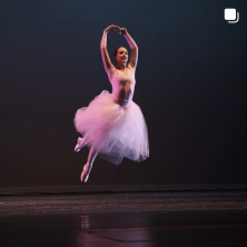 A ballerina hovers mid-air, arms raised above her head and toes pointed 