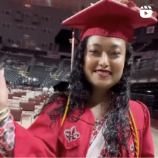 A UL Lafayette graduate in red robes at Commencement. Icon in corner indicates it is a video.