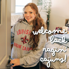 A UL Lafayette student opens the door of her dorm room while smiling at the camera.