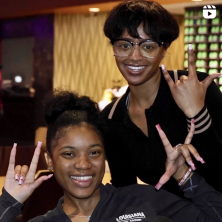 Two black-american female students sporting nice smiles and the ragin cajuns hand sign