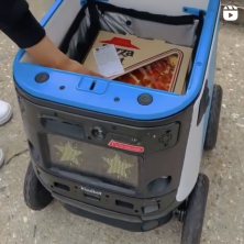 Picture of a student retrieving an order from the delivery robot "kiwi Bot"on campus