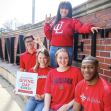 two male students alongside three female students in UL Lafayette branded red tshirts with a "Giving Day" sign