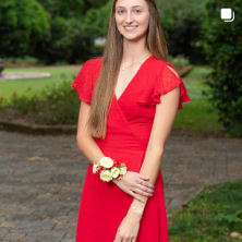 A white female student with long hair smiles. She wears a red dress and a wrist corsage.