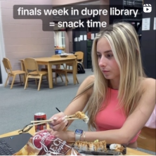 A UL student eating in the Dupre Library. A caption abover her head reading "finals week in dupre library = snack time"