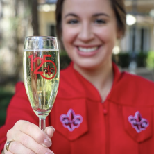 A woman holds out a champagne class with the UL 125 logo on it. 