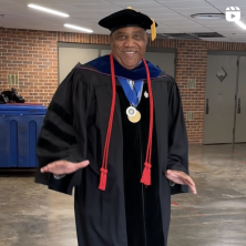 An older black man in an all black graduation robe dancing