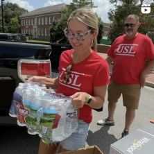 A woman in a USL shirt carring a pack of water bottles out of a pickup truck