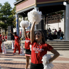 A cheerleader in read holding white pompoms dancing