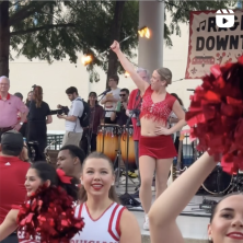 A group of cheerleaders, on of whom is holding a fire baton, dancing on a stage at Downtown Alive