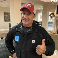 A man wearing a ragin cajun hat and a black weather channel shirt giving a thumbs up