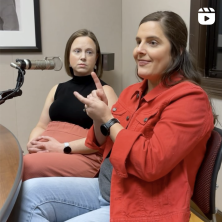 A woman in a red coat doing sign language during an interview