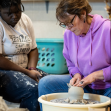 A woman in a purple hoodie sculpting clay