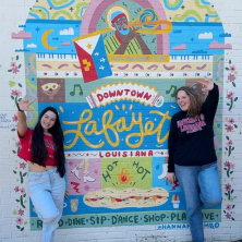 2 students standing in front of the downtown lafayatte mural