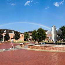 Student walks under rainbow arching the sky's campus