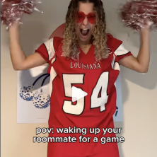 student wearing red Ragin Cajun merch shakes pom poms in excitement