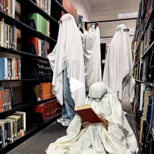 Four UL students with sheets over their heads pose with a bookshelf