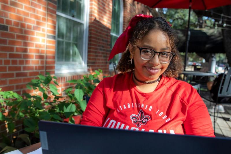 Courtney Johnson, wearing a red UL Lafayette shirt, sits outside at a coffee shop while working on her laptop.