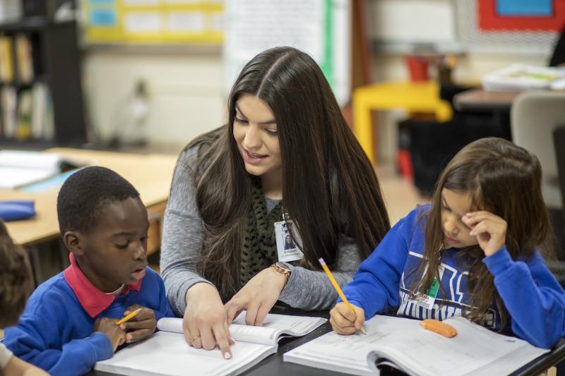 An education student helps two elementary students in their classroom.