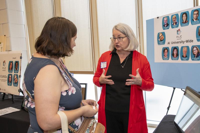 Instructional Technologist Renee Fiser is pictured in front of a research poster presentation as she speaks to a woman attending the FLC Showcase.