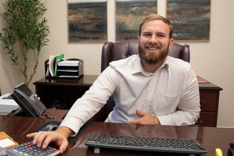 Dylan Chesterman, graduate of UL Lafayette's online master's in accounting, smiles while crunching numbers at his desk.