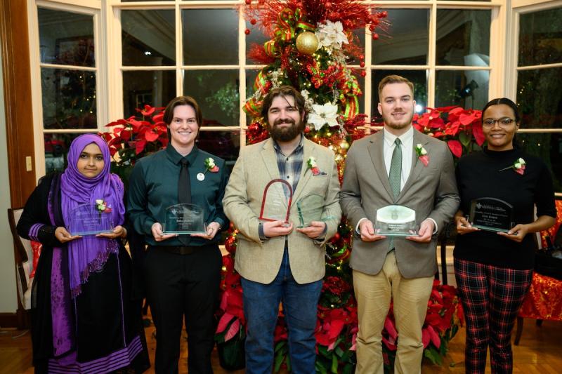 Five Outstanding Graduate master's students stand in front of a Christmas tree holding their awards.