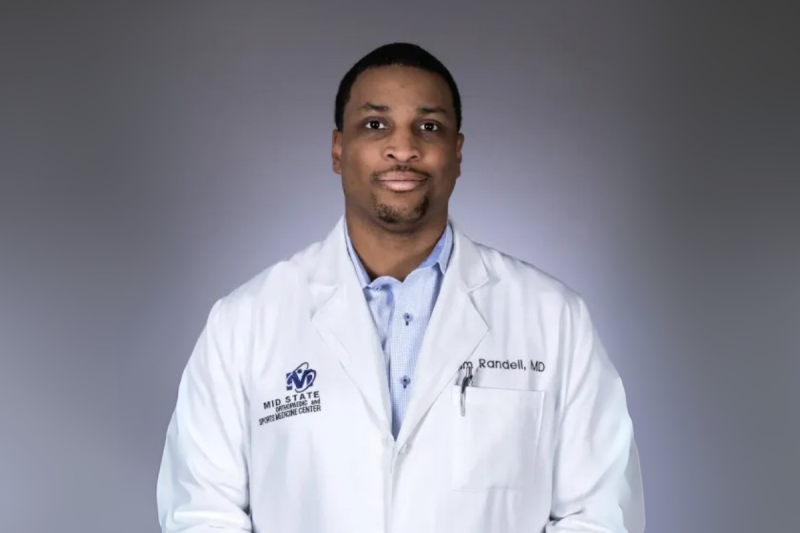 MBA in Health Care Administration online graduate smiles for headshot in white medical coat.