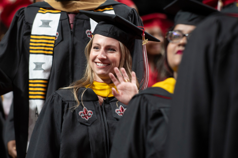 Online informatics graduate smiles and waves at her family, wearing UL Lafayette's black graduate-level cap and gown.