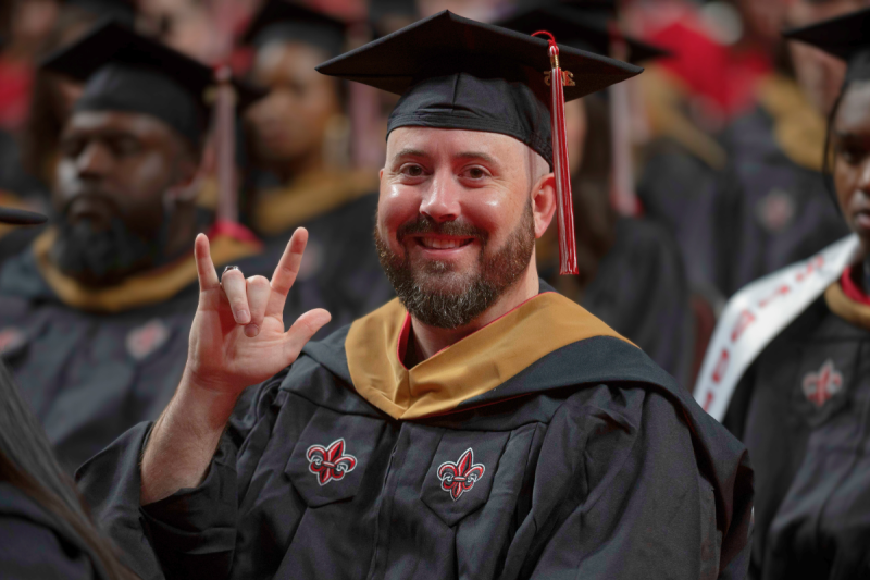 Brandon Hamilton, alumnus of UL Lafayette's MBA program online, holds up the U-L hand sign while seated at Commencement.