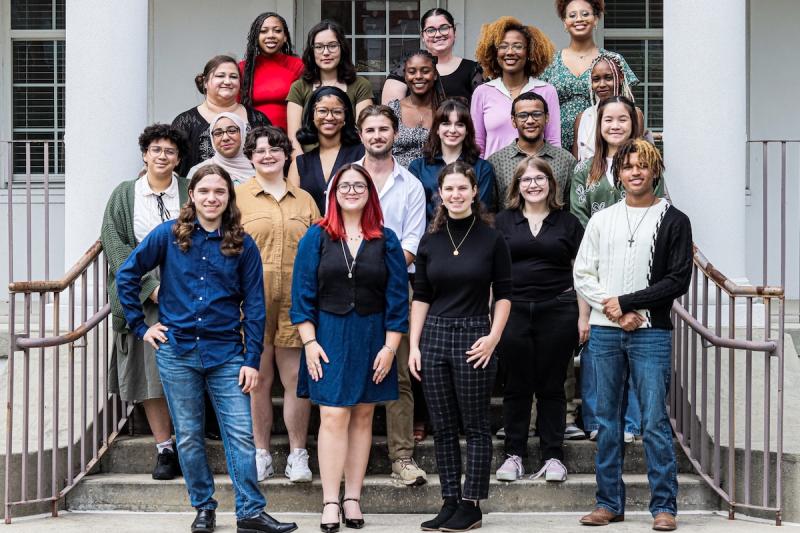 A group of students who work on the yearbook stand on the steps in front of a white house.