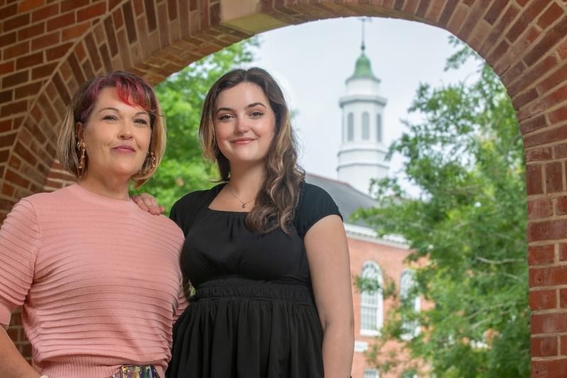 A woman in a pink sweater stands next to her daugher in a black blouse. Stephens hall is in the background.