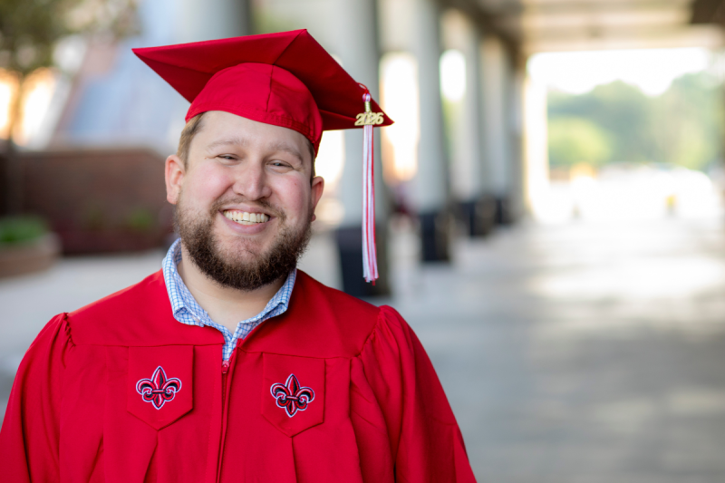 Graduate of the online management bachelor's degree program smiles in his cap and gown after graduating.