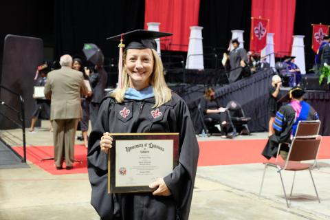 Erin Henry in her cap and gown with her master's degree plaque during Summer 2021 Commencement