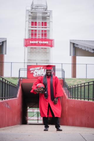 Tyrell Fenroy stands in Cajun Field, wearing his UL Lafayette graduation cap and gown.