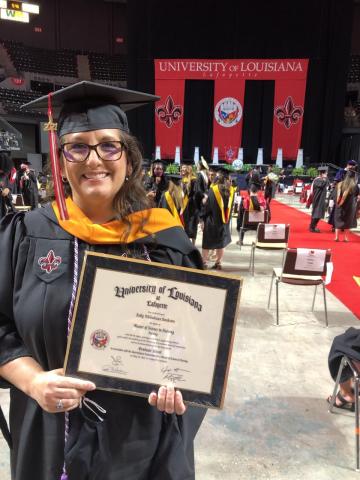Kelly Bankston, UL Lafayette MSN graduate, wears a black graduation cap and gown and holds her degree plaque during commencement exercises.