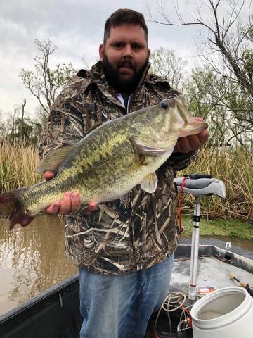 Photo of Zachary Badon wearing a camo jacket and holding a bass. Badon is earning his business degree online.