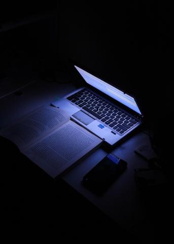 A laptop casts light over an open textbook.